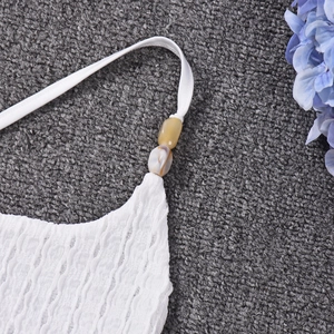Detail of white knit top featuring ribbed texture and amber-patterned decorative bead