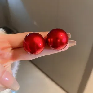 Glossy red round shell pearl stud earrings held between fingers for size reference