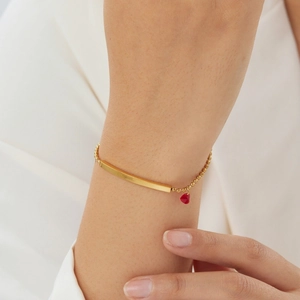 Close-up of gold beaded chain bracelet with red heart pendant worn by a model