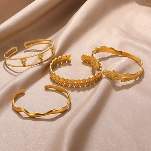 Detailed shot of four gold-plated hollow heart and leaf patterned open bangles on satin