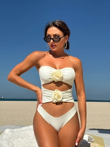 Close-up of a white cutout swimsuit with 3D floral rosettes on a beach background