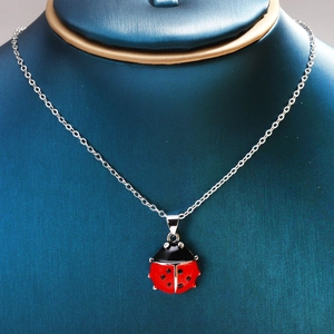 Detail of red and black ladybug pendant on a silver necklace displayed on a blue bust