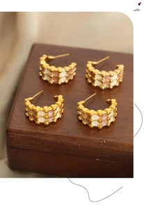 Detail of C-shaped geometric hoop earrings with check pattern enamel on a wood box