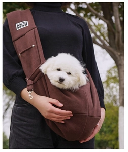 Outdoor photo of a model wearing a brown cotton pet sling bag with a small white puppy inside