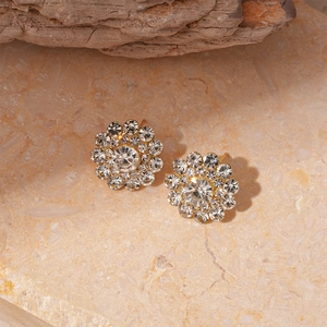 Macro detail of gold flower stud earrings with sparkling crystals on a stone surface