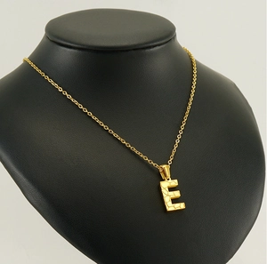 Detailed view of hammered 18K gold letter E pendant necklace on a black mannequin display
