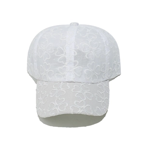 Dettaglio del ricamo in pizzo floreale bianco su berretto da baseball in rete da donna