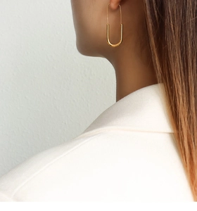Close-up of minimalist gold U-shaped earrings worn by a model in a white blazer