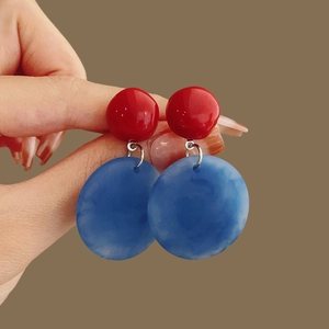 Detail shot of red resin stud earrings with blue circular teardrop pendants