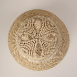 Close-up of woven straw sun hat featuring elegant white lace ribbon and faux pearl details