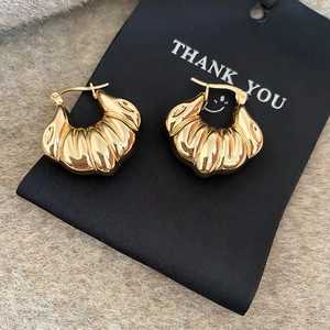 Detail of gold shell-shaped twist hoop earrings on a black card with beige plush background