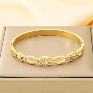 Goldener Evil-Eye-Armreif mit Zirkonia-Steinen auf einer edlen beigen Schmuckschatulle
