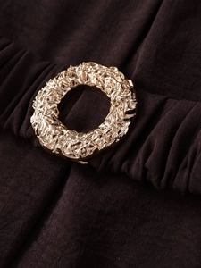 Detalle de hebilla de metal dorado martillado en tela plisada marrón para vestido playero