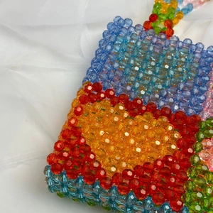 Close-up of colorful acrylic beads and orange heart pattern on a woven shoulder tote bag
