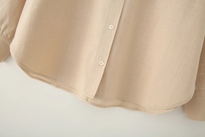 Detailed close-up of linen shirt hemline and white resin buttons in apricot color