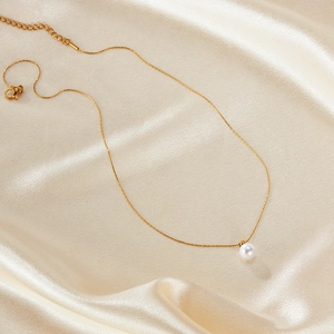 Elegant gold stainless steel necklace with round white pearl pendant on satin background