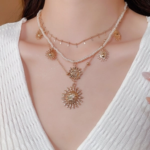 Close-up of triple-layered gold sun pendant necklace with pearls on a model wearing knitwear