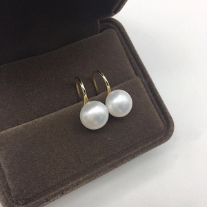 Macro detail of white freshwater pearls on golden ear hooks inside a jewelry box