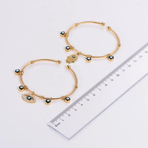 Detail of gold evil eye bangles featuring Hamsa Hand charm and twisted rope texture