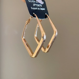 Close-up of golden geometric diamond pendant earrings with 925 silver needle hallmark