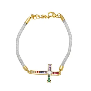 Detalle de pulsera con cruz bañada en oro y circonitas de colores en malla metálica