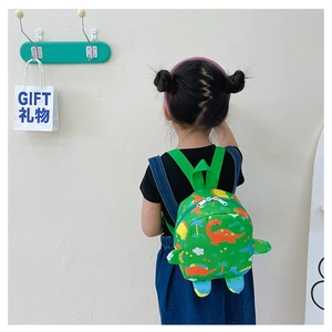 Rear view of a child wearing a green dinosaur print backpack against a white wall