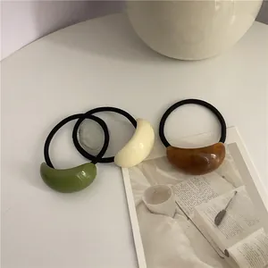 Close-up of three minimalist elastic hair ties with crescent-shaped resin accents in soft colors