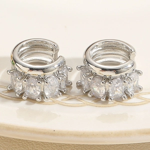 Macro detail of silver multi-layer ear cuffs with oval cubic zirconia on a cream plate