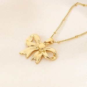 Elegant gold bow pendant necklace laid flat on a beige textured fabric background