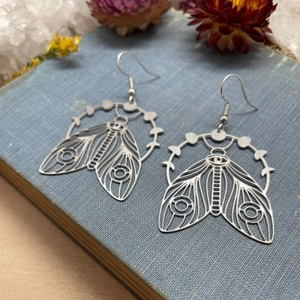 Bohemian silver cicada earrings with lunar phase cutouts on a vintage book backdrop
