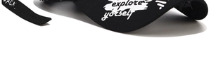 Detail of a black baseball cap featuring white graffiti print and explore yourself text