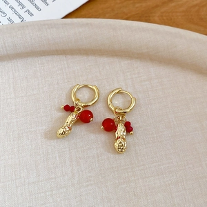 Detailed shot of golden peanut pendant earrings with red beads on a textured tray