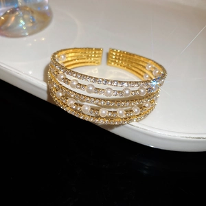 Close-up of a multi-layer gold cuff bracelet with sparkling zircon and elegant pearls