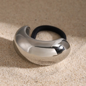 Detail of a high-shine silver metal hair buckle with a black elastic tie on sandy background
