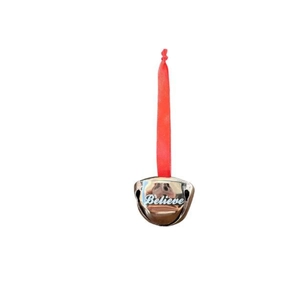 Macro view of metal Christmas bell with red ribbon and Believe engraving detail