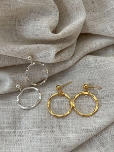 Detailed view of large gold and silver wavy hoop earrings on a textured beige linen fabric