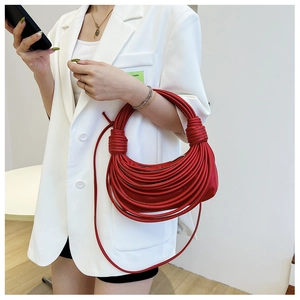 Dettaglio di una borsa a mano rossa intrecciata con corde di tessuto su blazer bianco