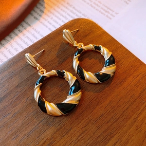 Macro detail of vintage gold and black enamel twisted hoop earrings on dark wood