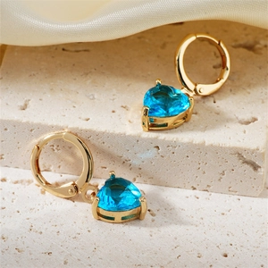 Eleganti orecchini a cuore dorati con gemma blu posati su una base di pietra grezza