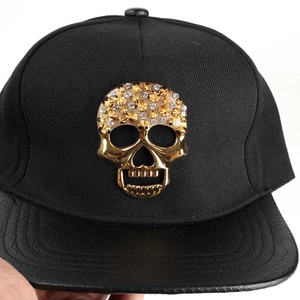 Détail du crâne en métal doré avec strass et visière en cuir de serpent sur la casquette