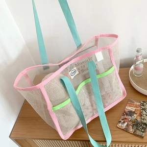 Detail of the mesh tote bag featuring pink trim and mint green handles on a wooden surface