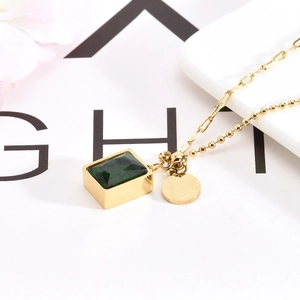 Detail of emerald green rectangular gemstone and gold coin pendant on mixed chain