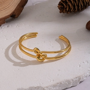 Minimalistisches Armband aus Edelstahl mit Knoten-Design auf weißem Steinhintergrund