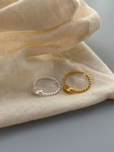 Close-up of minimalist gold and silver bead rings with heart charms on linen fabric