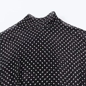 Dettaglio ravvicinato di una maglia nera a pois con collo alto in chiffon