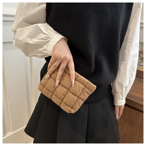 Detail of khaki quilted cosmetic bag with square stitching held by a model