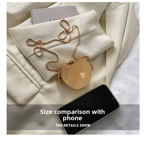 Mini gold heart-shaped crossbody bag with snake chain shown next to a smartphone