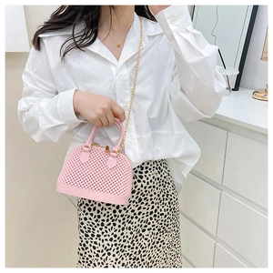 Detail view of a pink woven texture shell bag with golden metal chain on a model