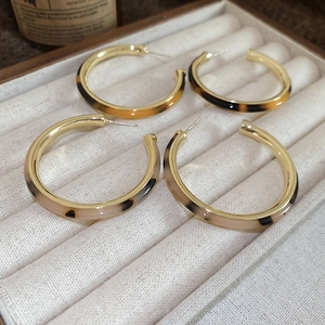 Detail of tortoiseshell patterned C-shape hoop earrings in dark amber and beige tones