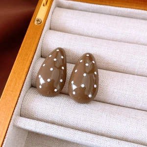Detail shot of brown water-drop earrings with white polka dots on beige velvet